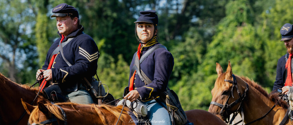 A female cavalry soldier on horseback, dressed in a Civil War-era uniform complete with a cavalry hat and riding gear. She exudes confidence and determination, representing the integral role of women in military history during this tumultuous period.